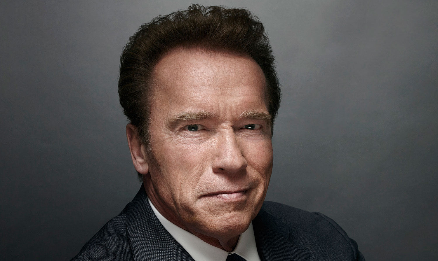 Arnold Schwarzenegger in a dark suit, looking at the camera