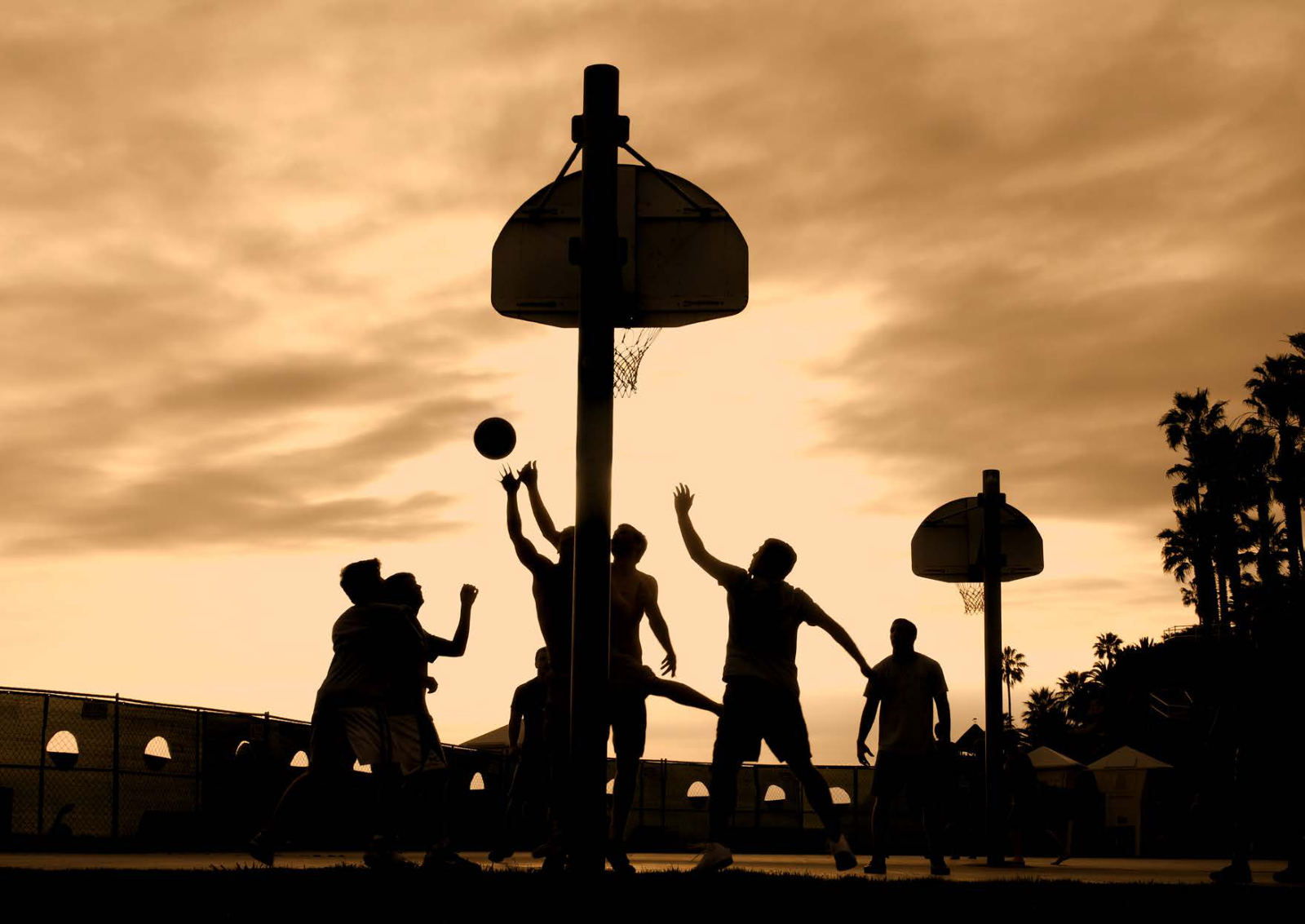 Silhouettes of players contesting a rebound on an outdoor court at sunset