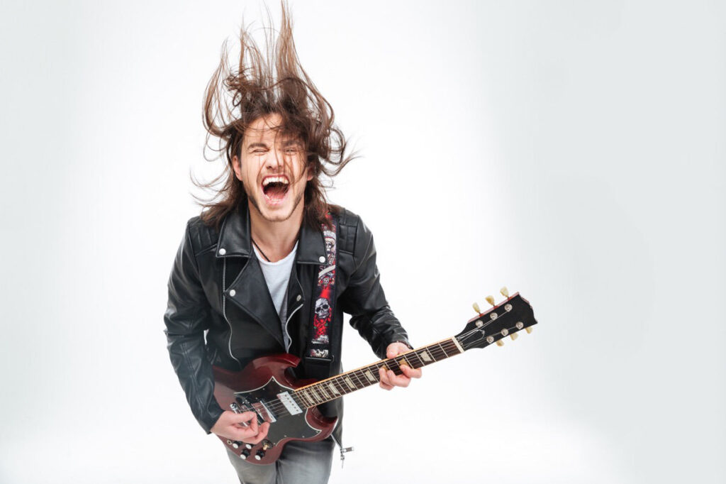 A young man with long hair leaping with an electric guitar