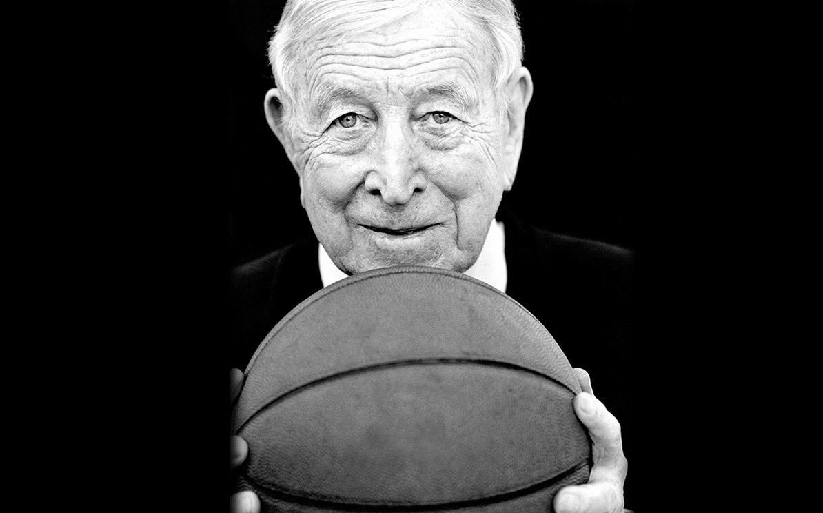 John Wooden, smiling, holding a basketball up to the camera