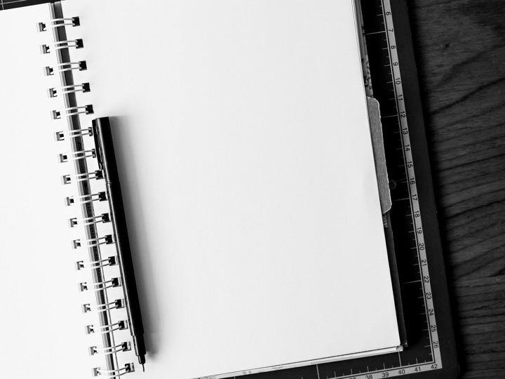 An open spiral notebook with a pen on a dark desk