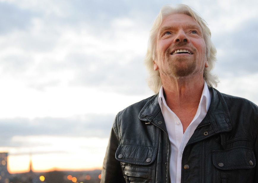 Richard Branson, smiling and looking up, in a leather jacket