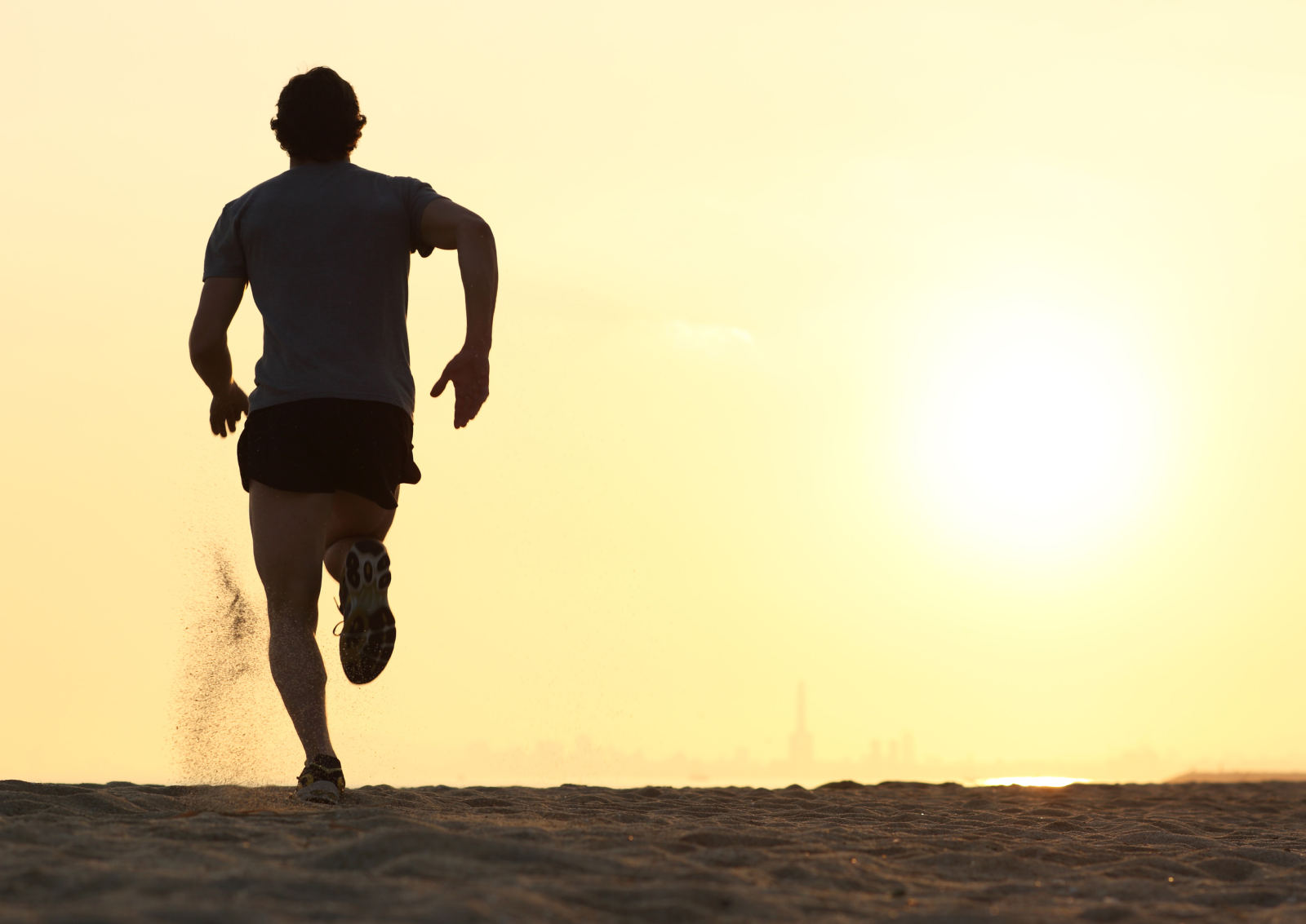 A runner silhouetted against a low sun on a beach