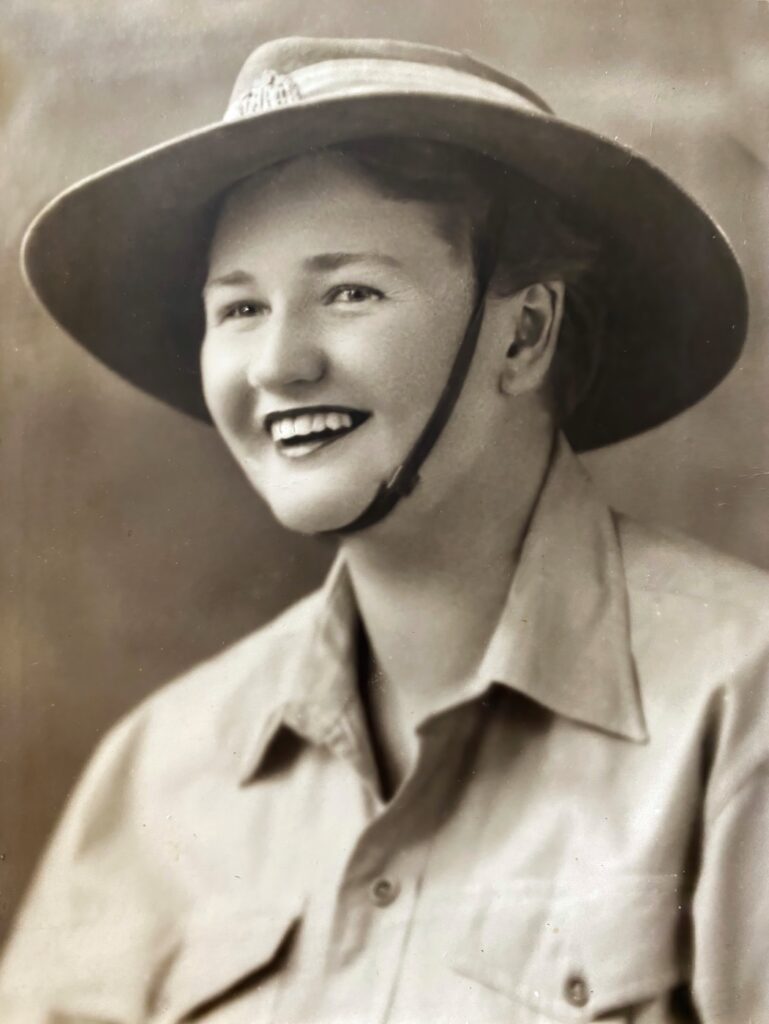 Meg Coten as a young woman, smiling, in a wide-brimmed hat and a collared uniform shirt